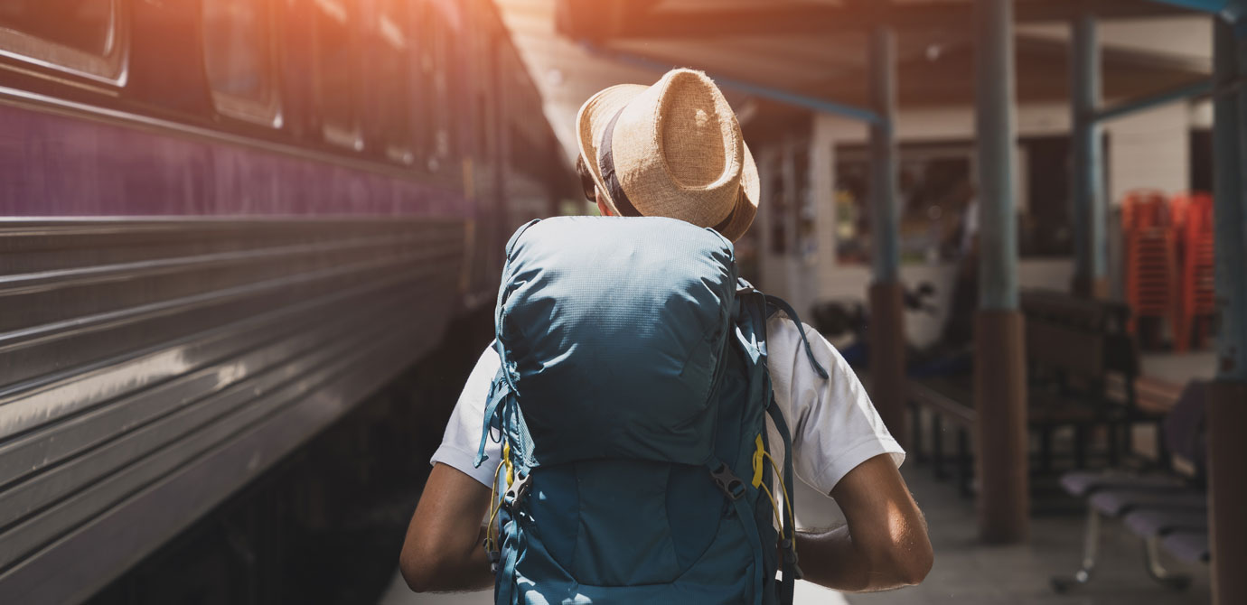 Insight_Content_Freiraumsucher Mann mit Rucksack und Strohhut von Hinten am Bahnhof